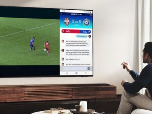 Un homme regarde un match de football sur sa télévision tout en lisant les nouvelles sur le même écran.